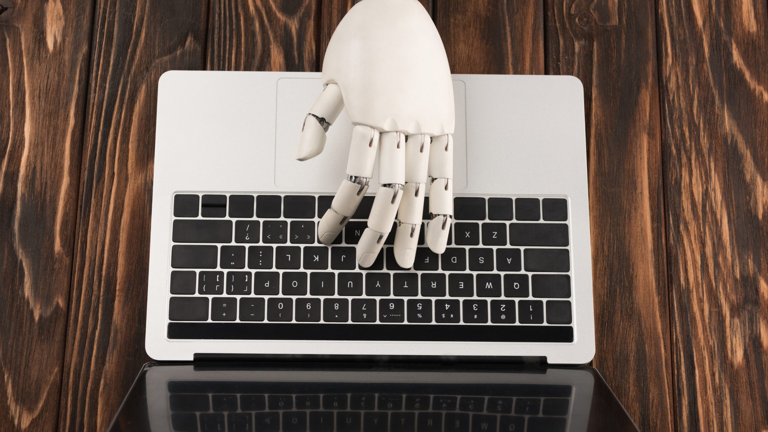 a white robotic hand typing on a MacBook Air representing AI in book marketing