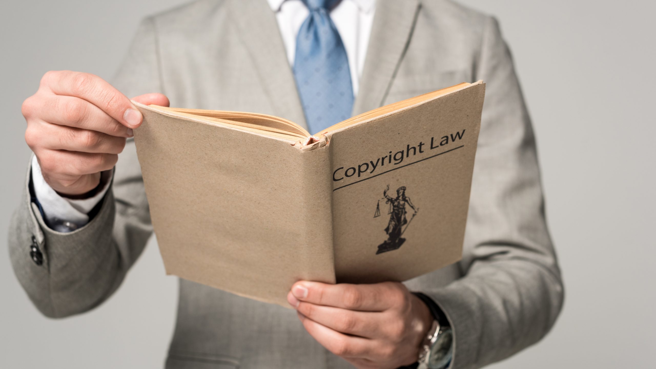 an frontal image of a person dressed in a beige suit with a blue tie reading up on fair use and coyright compliance for creatives