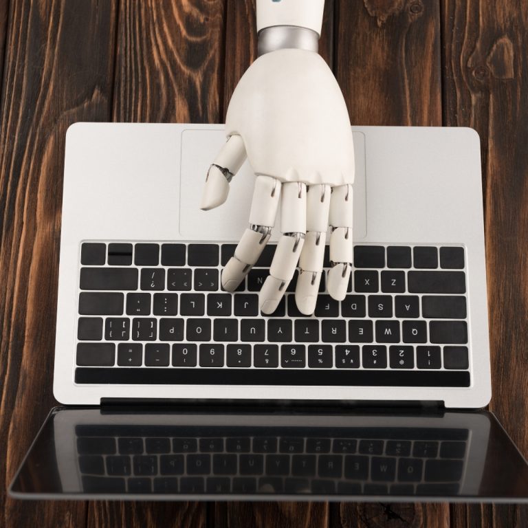 a white robotic hand typing on a MacBook Air representing AI in book marketing