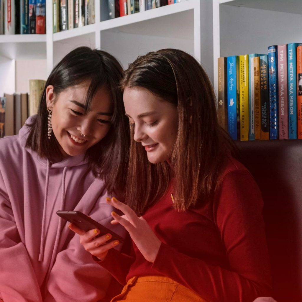 two girls sitting in front of a white bookshelf with books, reading public domain children's books online