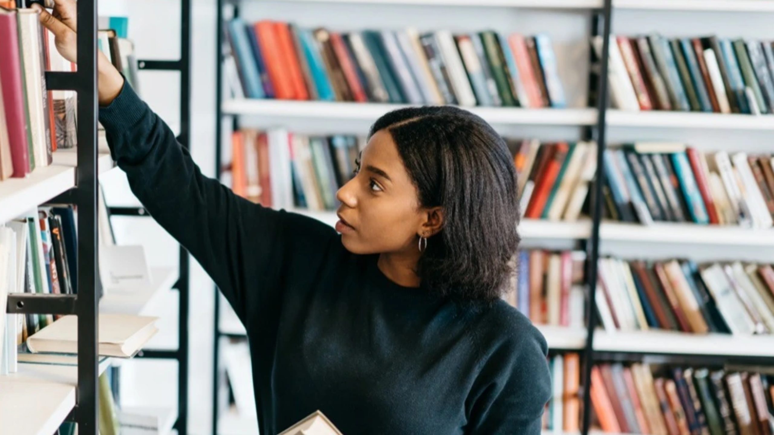 a woman browsing through a library filled with white book shelves contemplating how used book sales works online